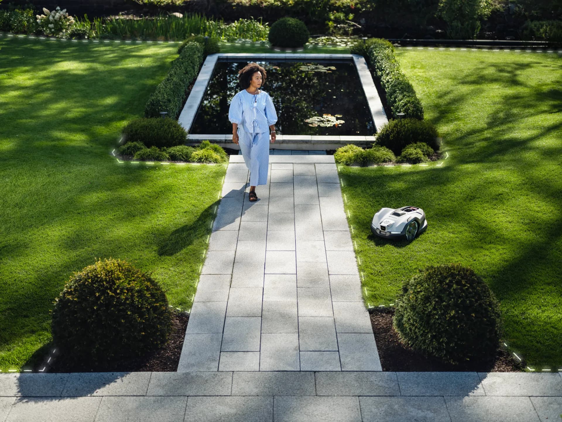 Jardin aménagé avec allée et bassin, un robot de tonte travaille sur la pelouse