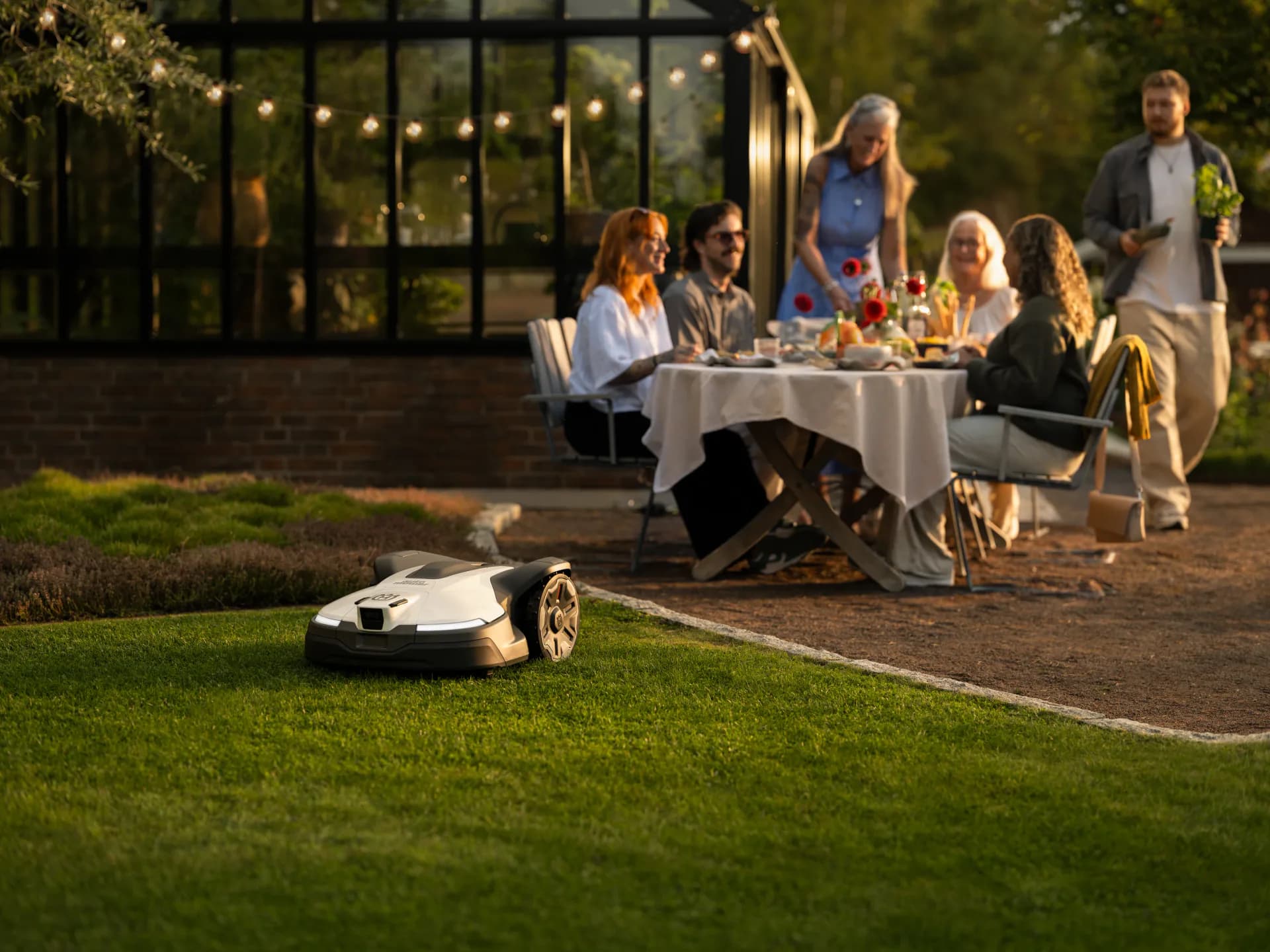 Garden party in the evening light, a robotic mower on the lawn in the foreground